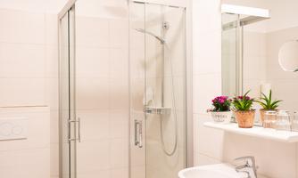 A modern bathroom with a glass shower stall. There are plants and towels on the sink.