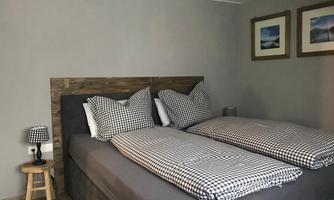 A cozy bedroom with two beds and checked pillows. Pictures hang on the wall and a small lamp stands next to the bed.