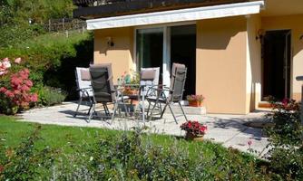 A beautiful outdoor area with a table and several chairs. Surrounded by colorful flowers and green lawn.