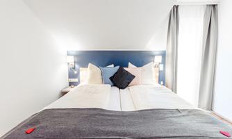 A cozy bedroom with a large bed and decorative pillows. The walls are painted in soft colors, and the lighting is pleasant and inviting.