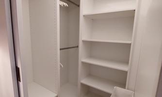 A clean, white cabinet with shelves and a hanging rod. The floor is made of wood and the cabinet appears spacious.