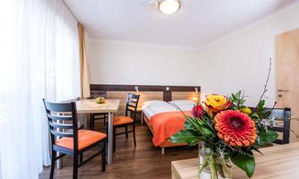 A modern room with a double bed and a table with chairs. On the table is a colorful bouquet of flowers.