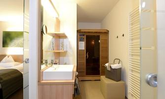A modern bathroom with a sink and a sauna. In the background, a cozy bedroom is visible.
