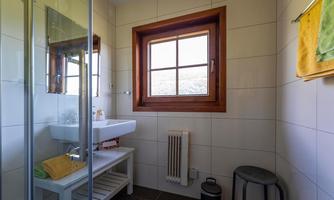 A modern bathroom with a shower, a sink, and a large window. It is bright and friendly designed with wooden elements.