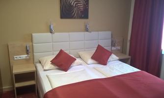 A cozy bedroom with a double bed and red pillows. The walls are painted in warm colors, and a picture of a zebra hangs on the wall.