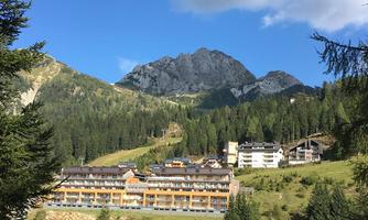 A picturesque mountain landscape with majestic peaks and dense forests. In the foreground, a modern accommodation is nestled in nature.