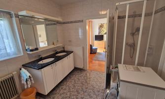 A modern bathroom with two sinks and a shower. The room is well-lit and has an elegant tiled floor.