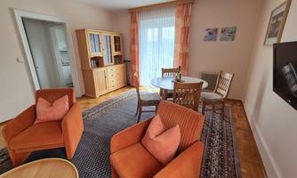 A cozy living room with orange armchairs and a round table. Large windows let in plenty of daylight and the carpet provides a warm ambiance.