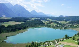 A picturesque landscape with a clear lake and gentle hills. In the background, majestic mountains rise under a blue sky.