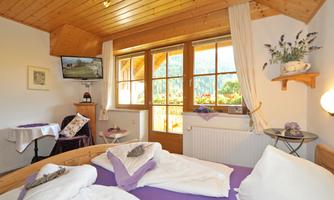 A cozy room with wooden walls and large windows. It is bright and inviting, with a large bed and a television.