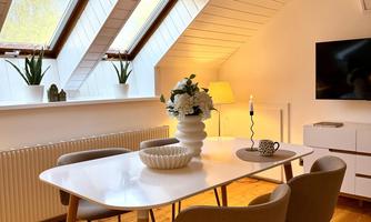 A cozy dining area with a white table and four chairs. Large windows let in plenty of daylight and create an inviting atmosphere.