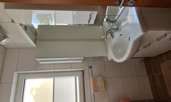 A modern bathroom with a white sink and mirrored cabinets. The light falls through a window, creating a bright atmosphere.