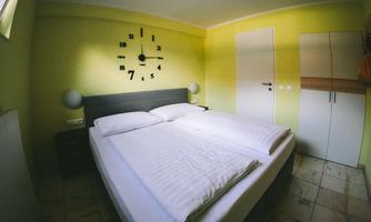 A cozy bedroom with a double bed and a modern clock on the wall. The walls are painted in a light yellow tone, creating a friendly atmosphere.