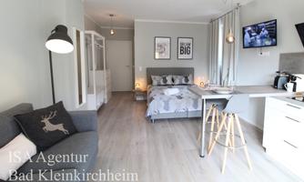 A modern, light-flooded apartment with a cozy bed and a small dining area. The decor is bright and inviting, ideal for a relaxing stay.