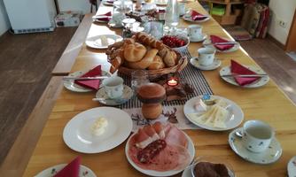 A beautifully set table with various foods, including rolls, cold cuts, and desserts. There are also cups and plates that invite to a cozy breakfast.