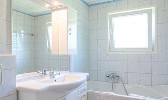 A modern bathroom with a bathtub and a sink. Bright tiles and a large window provide plenty of light.
