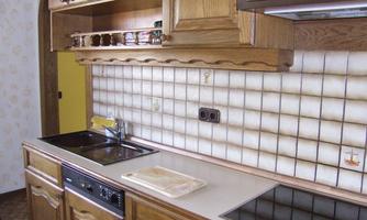 A modern kitchen with wooden cabinets and a bright countertop. The walls are decorated with square tiles in neutral colors.
