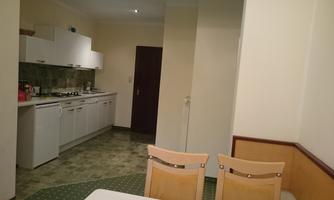 A simple kitchen with modern appliances and a dining area. The walls are painted light and the floor is covered with linoleum.