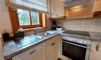 A modern kitchen with wooden details, a sink, and a stove. The window lets in a lot of daylight.