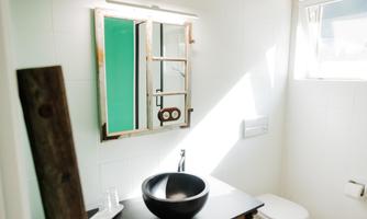 A modern bathroom with a large vanity and a round sink. Natural light flows through a window and highlights the bright walls.