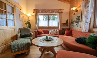 A cozy living room with a large, round table and a comfortable, red couch. The wood decor and the windows create a warm and inviting atmosphere.