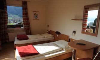 A simple room with two beds and a table. The window offers a view of the surrounding landscape.