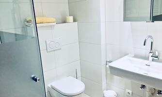 A modern bathroom with white tiles. It includes a toilet, a sink, and a shower.