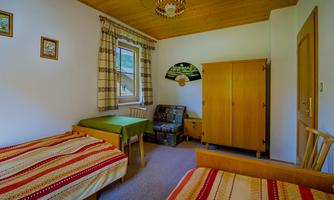 A cozy room with two beds and a table. The walls are light, and the furniture is made of wood.