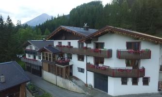 A beautiful house in the mountains with balconies and floral decorations. Surrounded by trees and a gentle hill in the background.
