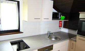 A modern kitchen with white cabinets and a stainless steel countertop. It is well-lit and has basic kitchen appliances.
