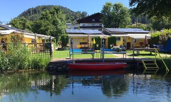 A picturesque approach to a body of water with a red boat in the foreground. In the background, cozy yellow houses and lush greenery are visible.