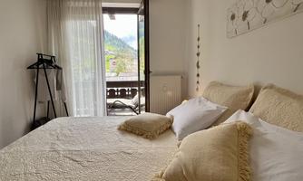 A bright bedroom with a large bed and elegant decorative pillows. The view of the balcony offers a beautiful sight into the greenery.