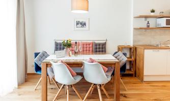 A modern dining area with a wooden table and colorful chairs. In the background, there is an open kitchen and pleasant lighting.