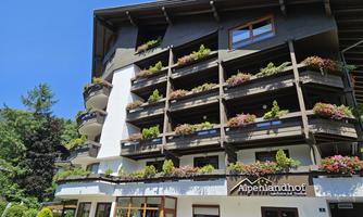 A charming hotel with blooming balconies and a clear blue sky. The facade is friendly and inviting.