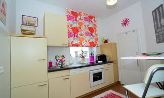 A modern kitchen with bright cabinets and colorful curtains. On the countertop, kitchen utensils and a window with a view outside can be seen.