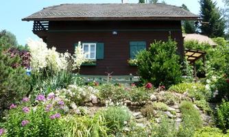 A cozy wooden house surrounded by colorful flowers and green plants. The garden is well-maintained and invites you to linger.