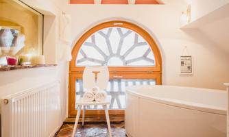 A bright bathroom with a large, round window. In the corner, there is a bathtub and a chair with towels.