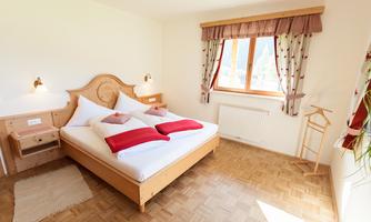 A bright room with a large double bed and red pillows. A window offers a view of the outdoor area and lets in plenty of daylight.