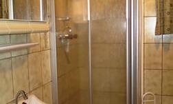 A simple bathroom with a shower cubicle and a sink. The walls are tiled and there is a small rug on the floor.