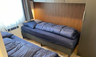 A modern bedroom with two single beds and a warm wood paneling. The window lets in plenty of daylight, making the space feel inviting.