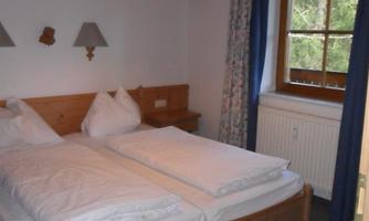 A cozy bedroom with two single beds and wooden details. The window offers a view of the greenery.