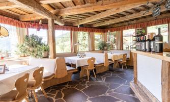 A cozy restaurant with wooden furniture and large windows. The room is bright and inviting, with a rustic ambiance.