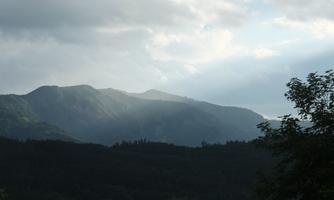 A picturesque mountain landscape under a cloudy sky. Gentle rays of light fall on the mountains, creating a tranquil atmosphere.