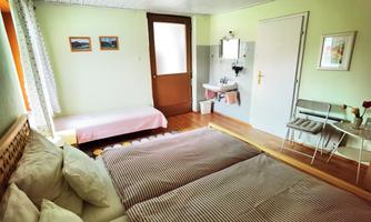 A bright bedroom with two single beds and an additional bed. There are some pictures hanging on the wall, and there is a sink in the room.