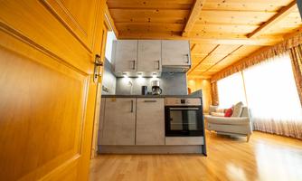 A modern kitchen with wooden shelves and a cooktop. Bright room with a cozy sofa in the background.