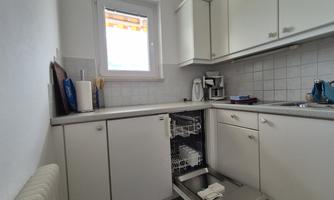 A modern kitchen with white cabinets and a dishwasher. There is also a large window and various kitchen appliances on the countertop.