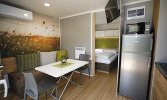 A modern room with a kitchenette, dining table, and a cozy sleeping area. The decor is bright and friendly, with simple furniture and a beautiful mural.