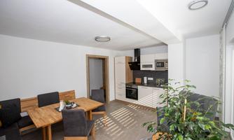 A modern kitchen with a dining table and chairs. The design is bright and open, with a plant in the corner.