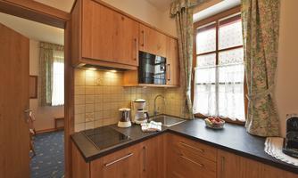 A cozy kitchen with wooden cabinets and modern appliances. The window is decorated with curtains, and there is fresh fruit as well as a coffee machine on the countertop.