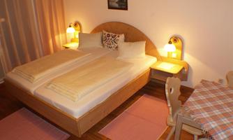 A cozy bedroom with a double bed and a wooden frame. Next to the bed are nightstands with lamps and a small table with chairs.
